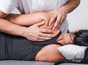 Physical therapist works with woman's shoulder